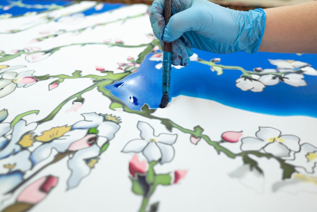 Applying dark blue color to a white silk scarf with a floral pattern using a brush, batik