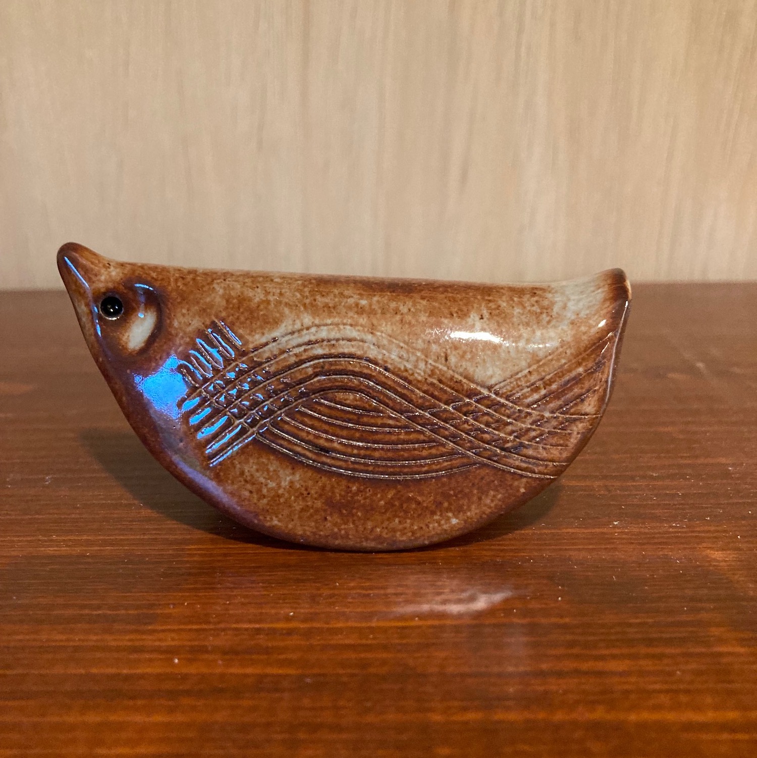 Small brown clay bird on a dark brown shelf with a light brown background